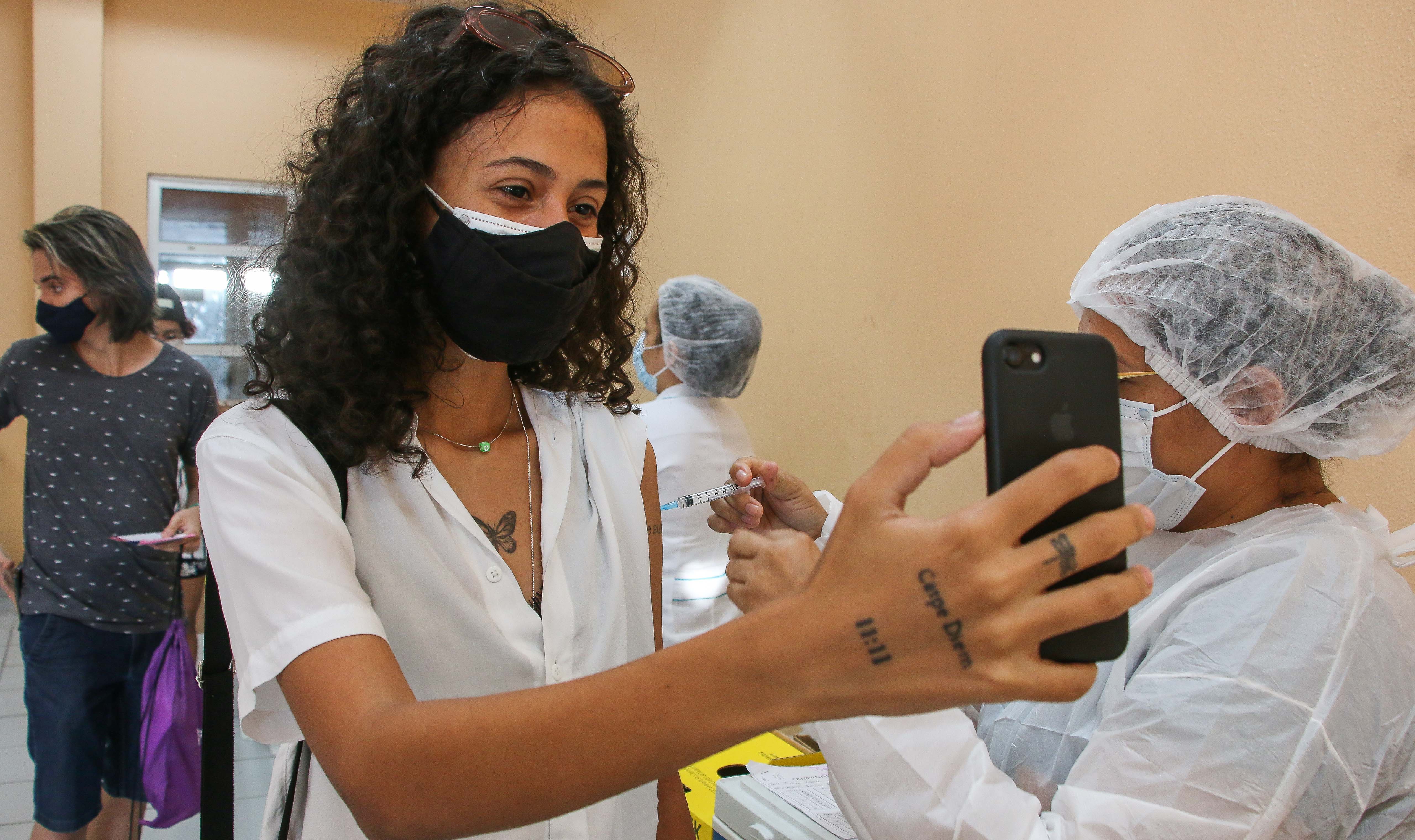 uma jovem tira um selfie enquanto é vacinada